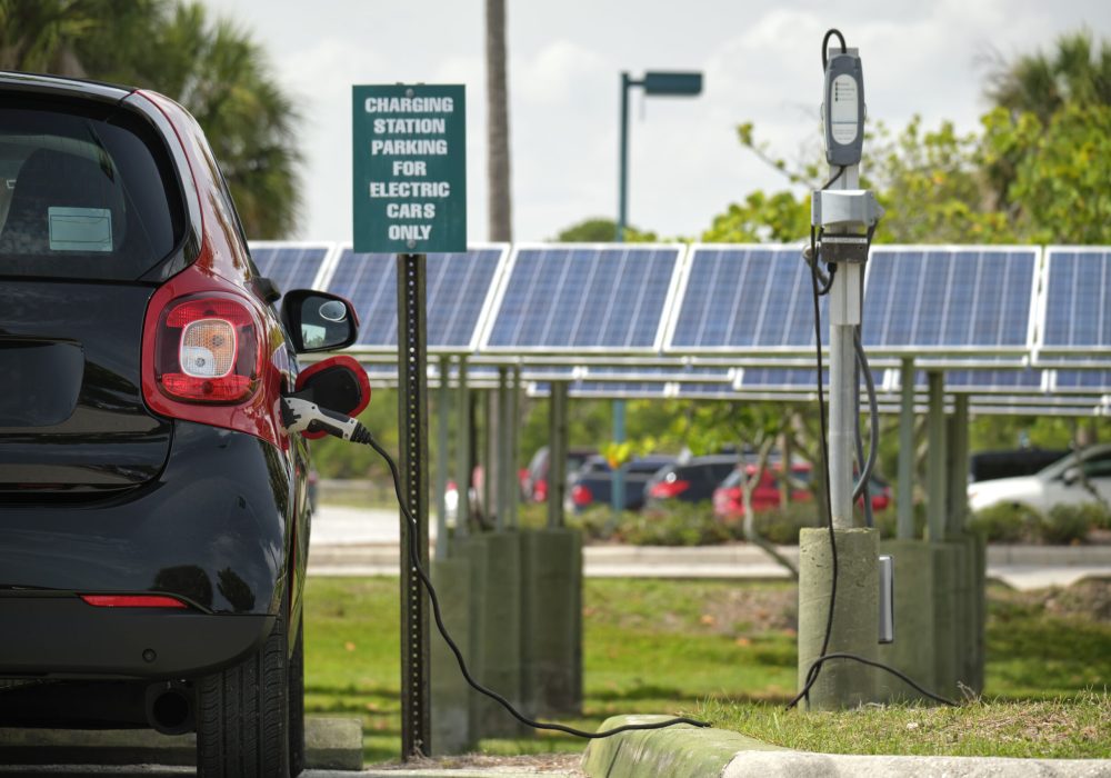 Electric plug-in car charging with electricity from solar renewable power source parked on city street.